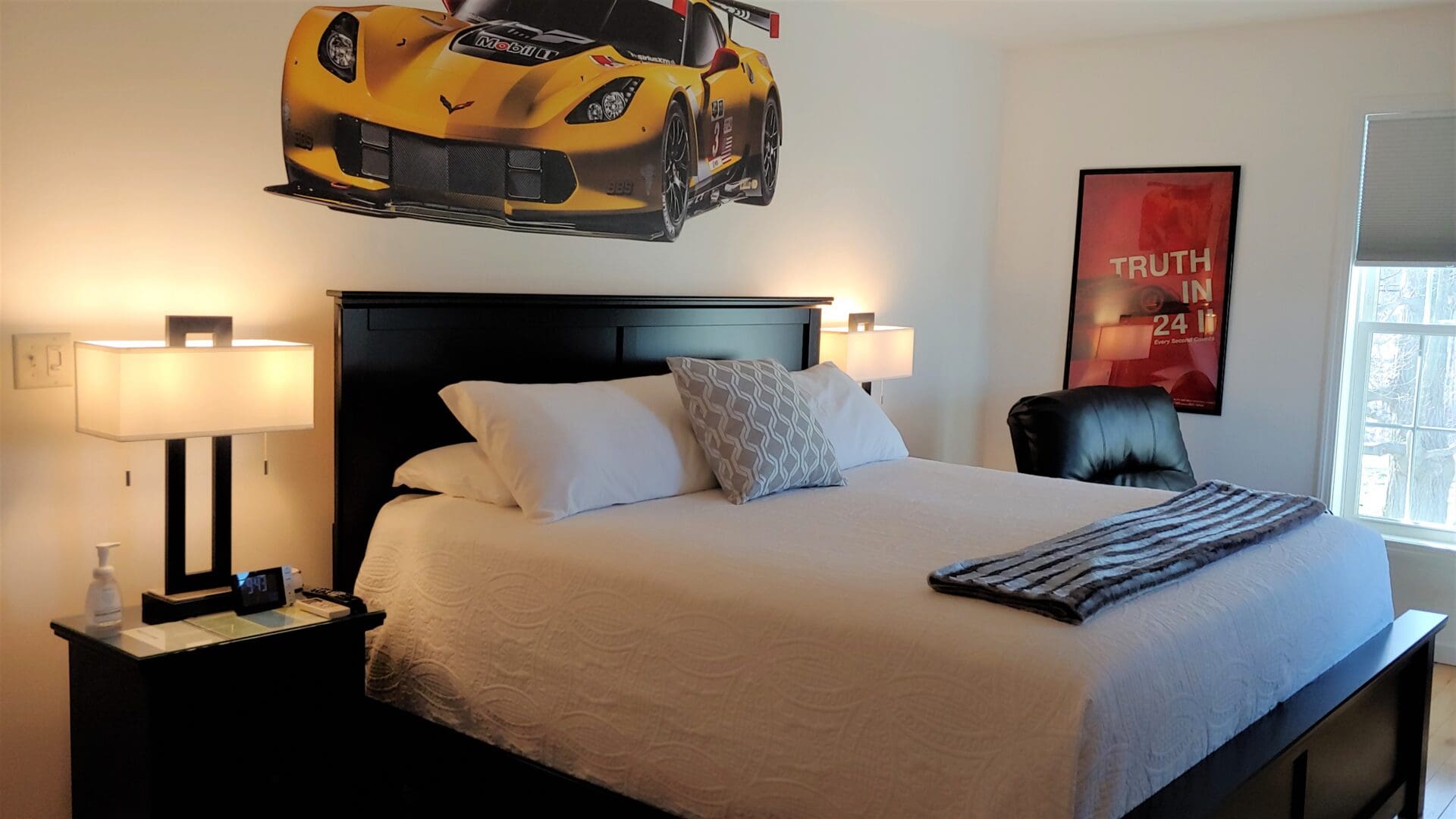 A bedroom with a bed, chair and a yellow car on the wall.